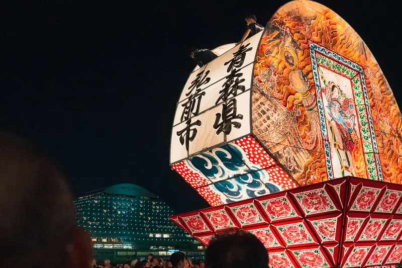 ねぷたの上で作業するスタッフと背後の夜景