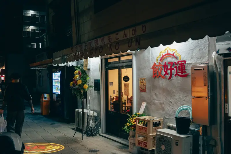 夜の餃好運の外観。開店祝いの花が並ぶ