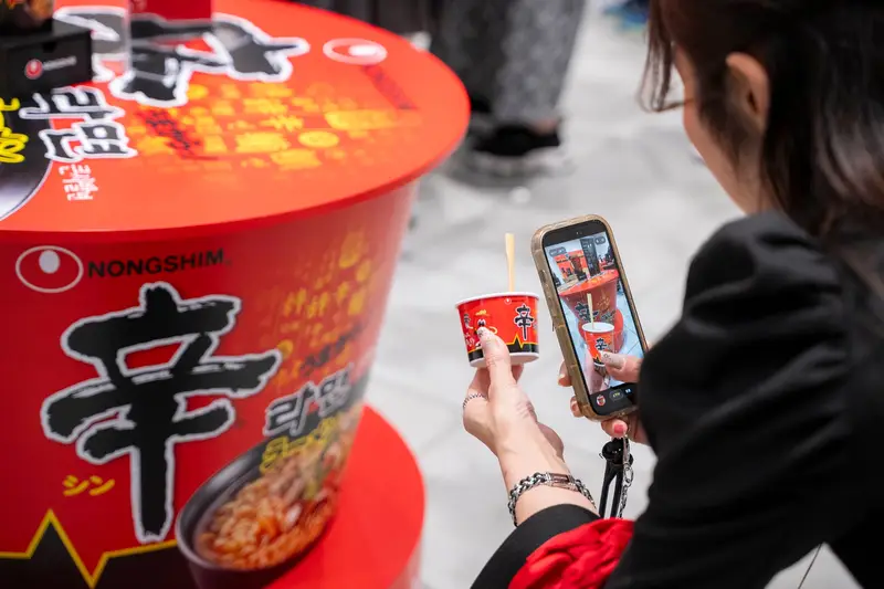 辛ラーメンのカップを手にスマートフォンで撮影する来場者