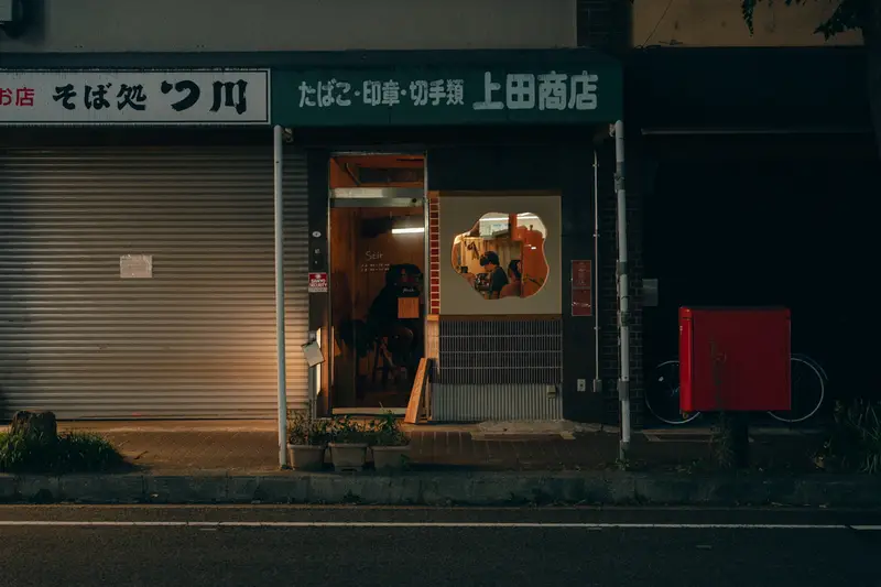 「たばこ・印紙・切手類 上田商店」の看板が残る stir の外観（夜）
